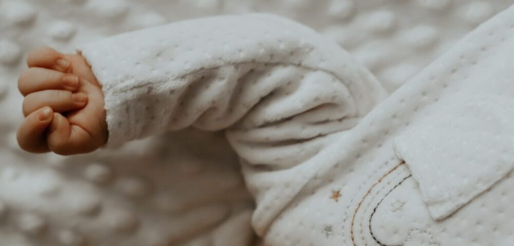 baby in white onesie lying on white textile